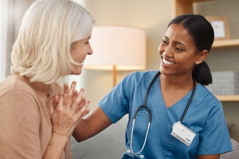 Caring staff member assisting an older adult with daily activities in a bright, home-like common area.